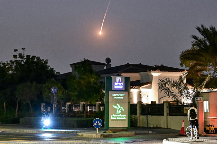 A cyclist watches a bright projectile falling through the dark sky over Dubai.